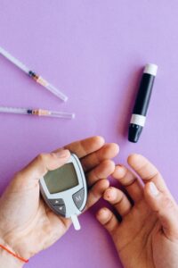 Person holding glucose meter with syringes on a purple surface, health concept.
